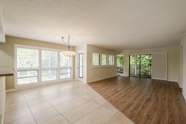 unfurnished living room featuring a notable chandelier, a textured ceiling, and light tile patterned floors