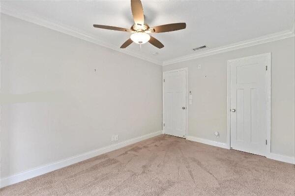 empty room featuring crown molding, light colored carpet, and ceiling fan