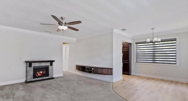 unfurnished living room with ceiling fan with notable chandelier, a stone fireplace, light colored carpet, and crown molding