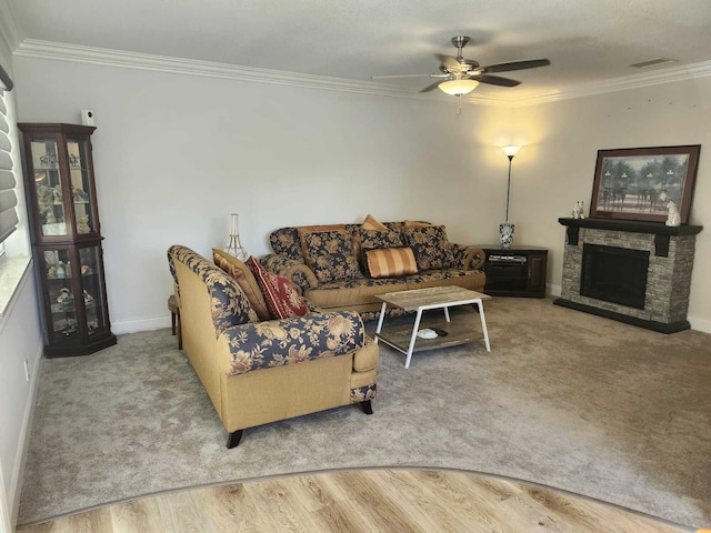 living room with ceiling fan, a stone fireplace, and crown molding