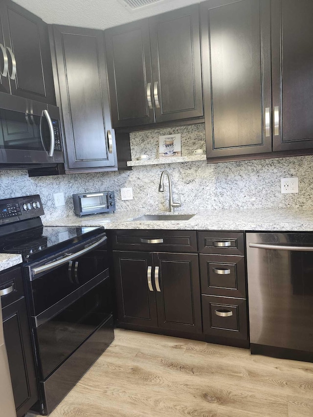 kitchen with dark brown cabinetry, sink, stainless steel appliances, light stone counters, and light hardwood / wood-style flooring