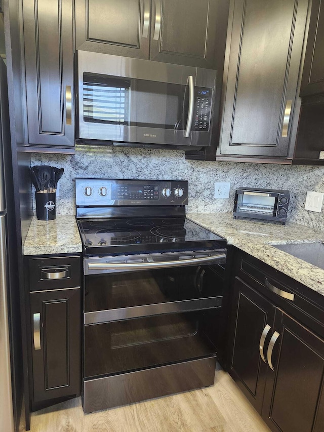 kitchen featuring light stone countertops, appliances with stainless steel finishes, light wood-type flooring, and tasteful backsplash