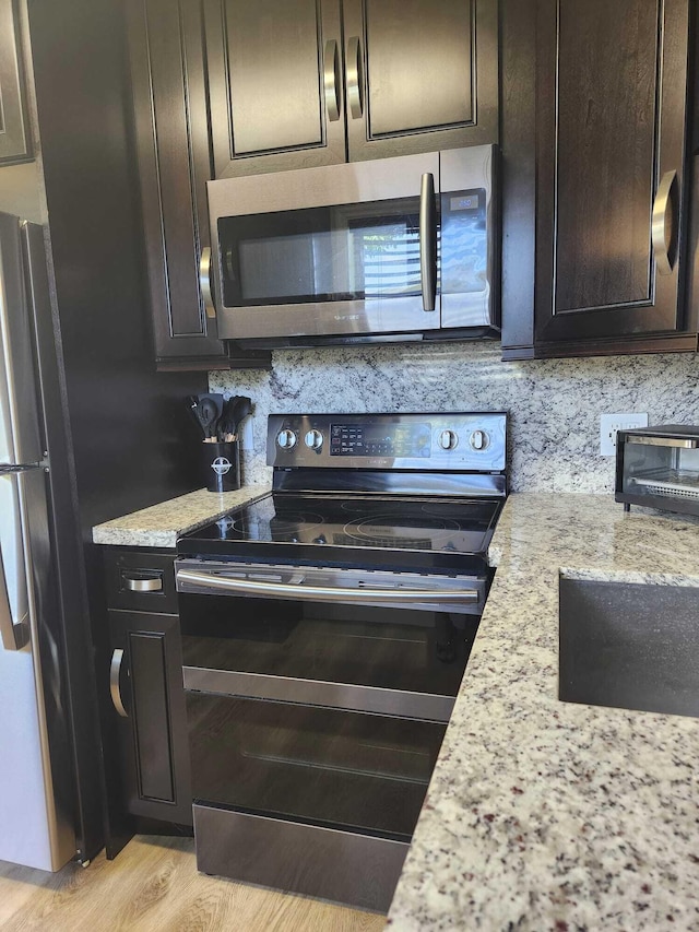 kitchen featuring appliances with stainless steel finishes, light wood-type flooring, light stone counters, and dark brown cabinetry