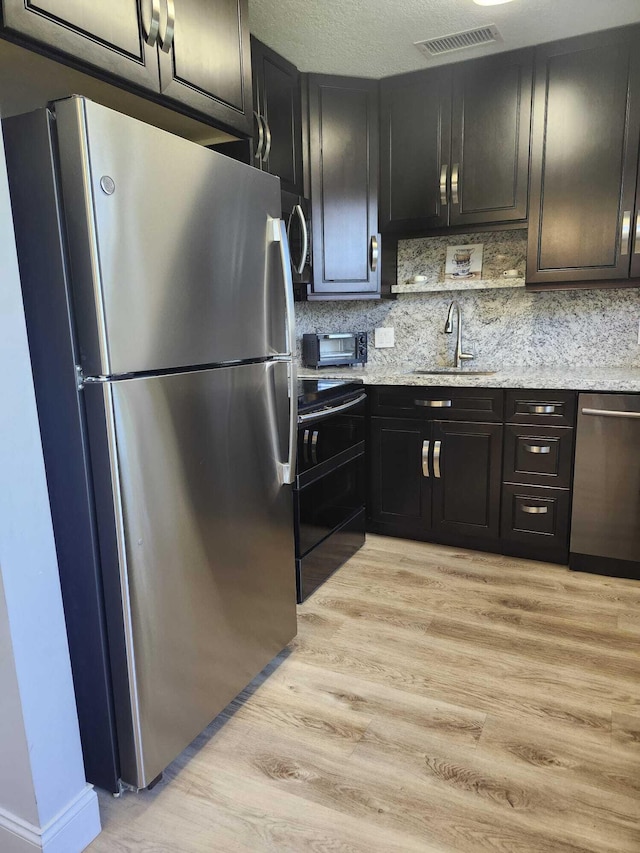 kitchen featuring stainless steel appliances, light hardwood / wood-style floors, sink, and light stone countertops