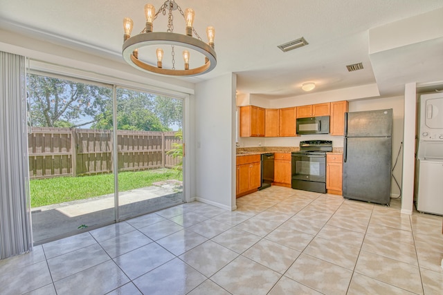 kitchen featuring stacked washer and dryer, light tile patterned flooring, black appliances, and an inviting chandelier