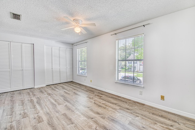 unfurnished bedroom featuring two closets, multiple windows, light hardwood / wood-style flooring, and ceiling fan