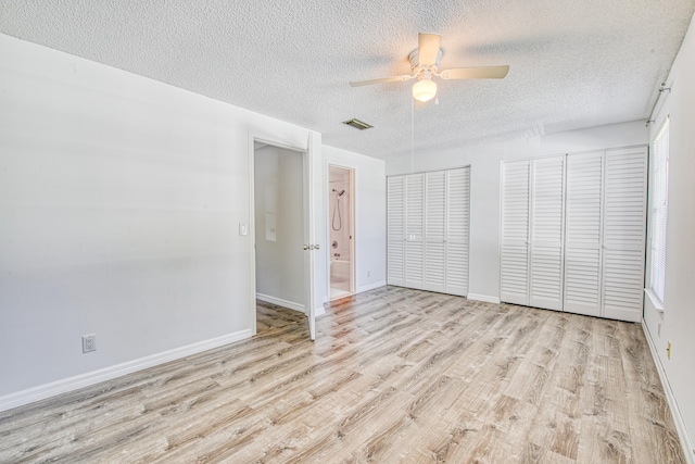 unfurnished bedroom with two closets, light hardwood / wood-style floors, a textured ceiling, and ceiling fan