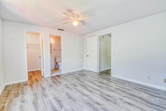 unfurnished bedroom with a closet, a spacious closet, ceiling fan, ensuite bathroom, and a textured ceiling