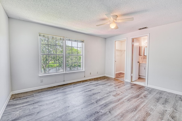 unfurnished bedroom featuring a textured ceiling, ceiling fan, a walk in closet, a closet, and ensuite bath