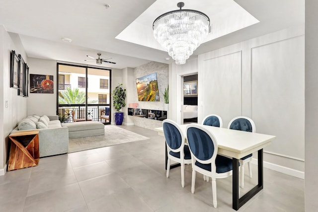 dining room with a tray ceiling, expansive windows, light tile patterned floors, and ceiling fan with notable chandelier