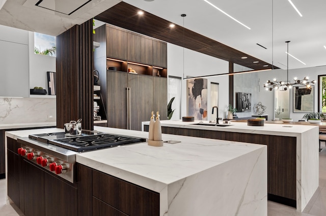 kitchen with stainless steel gas stovetop, decorative light fixtures, a large island with sink, and sink