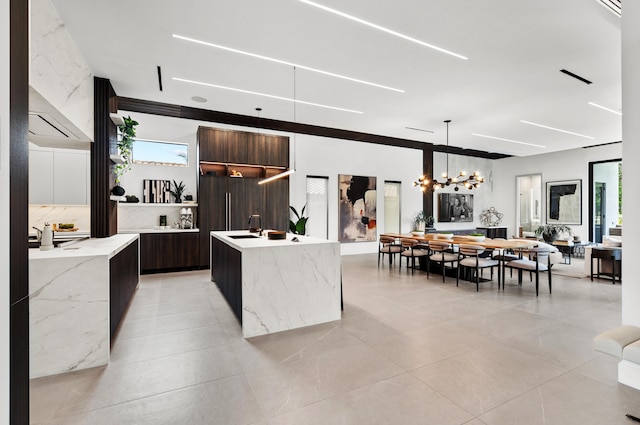 kitchen featuring sink, decorative light fixtures, a kitchen island with sink, an inviting chandelier, and light stone countertops