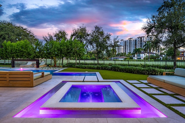 pool at dusk featuring an in ground hot tub and a patio area