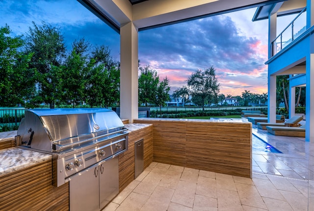 patio terrace at dusk featuring exterior kitchen and area for grilling