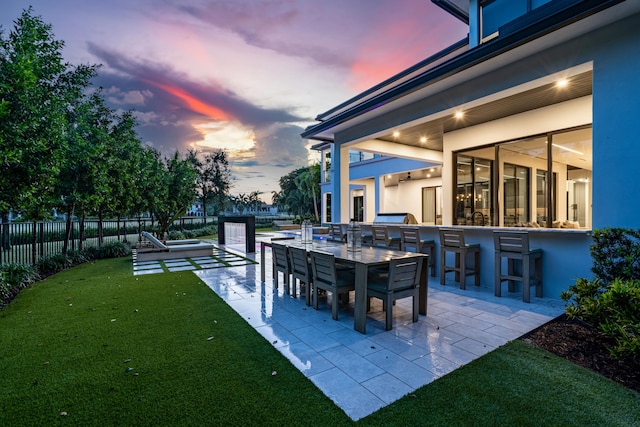 patio terrace at dusk with exterior bar, a lawn, and exterior kitchen