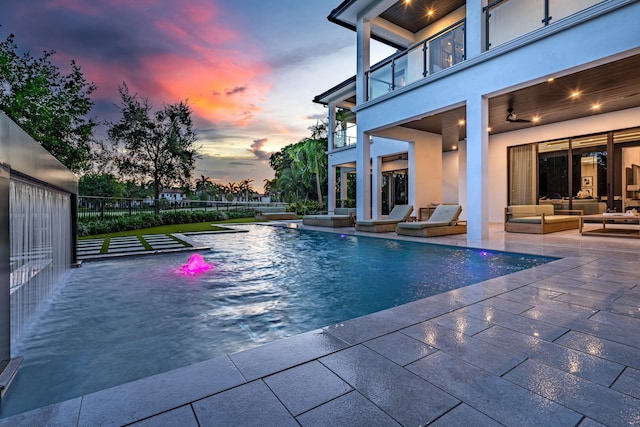 pool at dusk featuring ceiling fan, outdoor lounge area, and a patio area