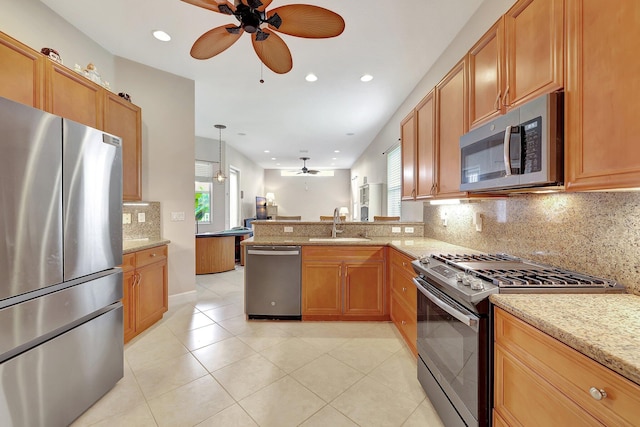 kitchen featuring sink, appliances with stainless steel finishes, light stone counters, decorative light fixtures, and kitchen peninsula