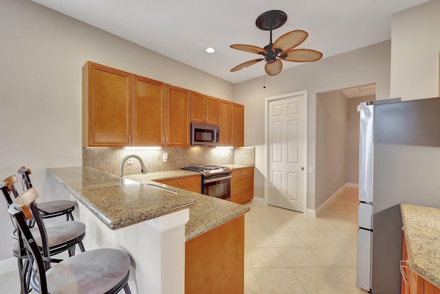 kitchen featuring sink, appliances with stainless steel finishes, light stone countertops, a kitchen bar, and kitchen peninsula