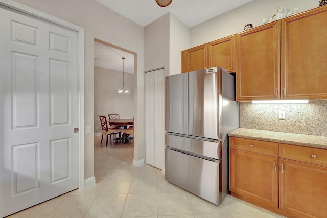 kitchen with stainless steel refrigerator, decorative light fixtures, tasteful backsplash, light tile patterned floors, and light stone countertops