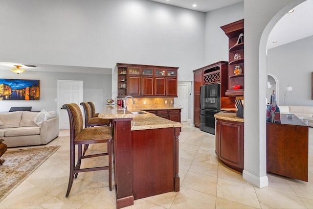 kitchen with a kitchen breakfast bar, sink, decorative backsplash, light stone counters, and black fridge