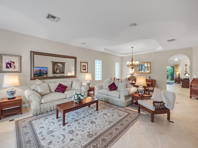 living room featuring light tile patterned flooring, plenty of natural light, a tray ceiling, and an inviting chandelier