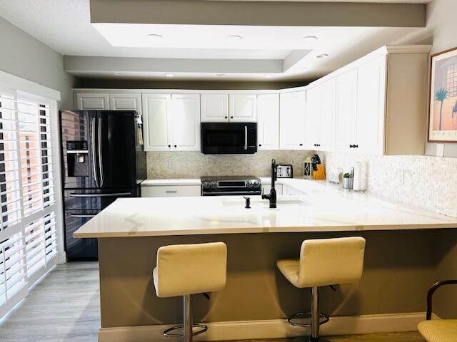 kitchen with black appliances, decorative backsplash, and a breakfast bar area