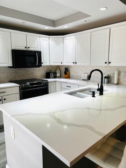 kitchen with black appliances, a tray ceiling, white cabinets, and decorative backsplash