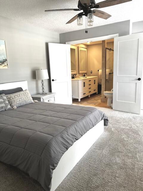 bedroom featuring connected bathroom, ceiling fan, a textured ceiling, and light colored carpet