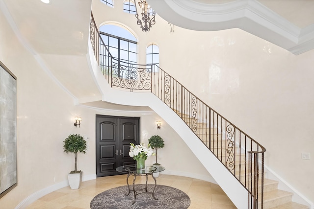 entrance foyer with light tile patterned flooring, a chandelier, crown molding, and a towering ceiling