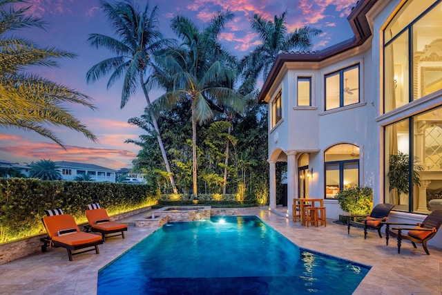 pool at dusk with an in ground hot tub and a patio area