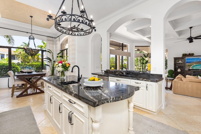 kitchen with sink, dark stone countertops, coffered ceiling, and a kitchen island with sink