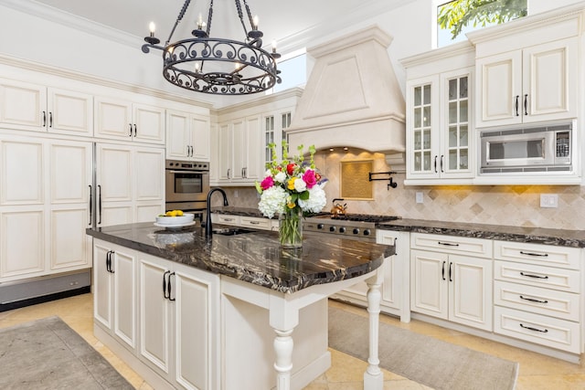 kitchen with tasteful backsplash, stainless steel appliances, sink, custom range hood, and a kitchen island with sink