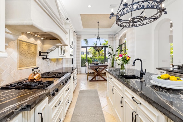 kitchen featuring white cabinetry, a tray ceiling, decorative backsplash, sink, and custom range hood