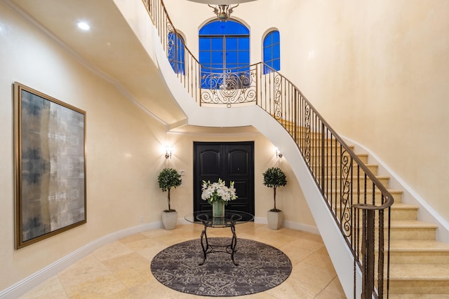 entryway with a towering ceiling, tile patterned floors, and ornamental molding