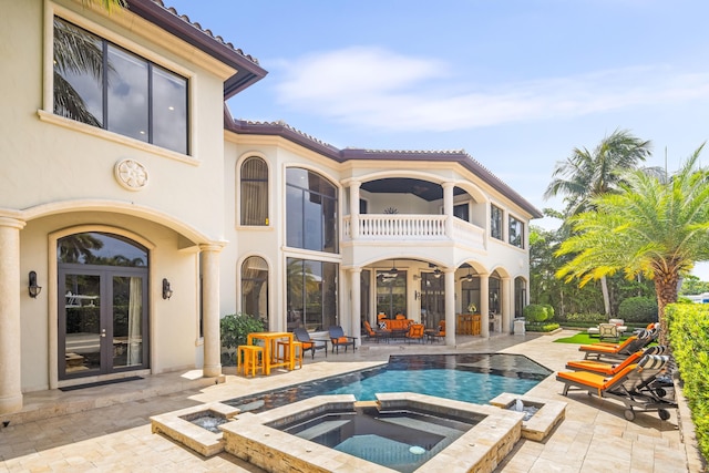 rear view of property featuring a swimming pool with hot tub, a patio, and a balcony