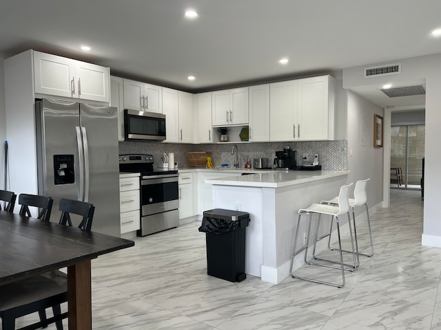 kitchen featuring a breakfast bar area, light tile patterned floors, white cabinets, backsplash, and stainless steel appliances