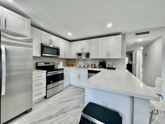 kitchen with appliances with stainless steel finishes, a breakfast bar, kitchen peninsula, backsplash, and light tile patterned flooring