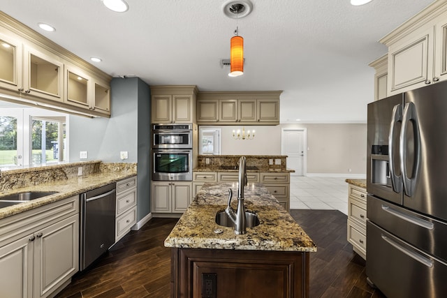 kitchen with sink, hanging light fixtures, stainless steel appliances, cream cabinets, and a center island with sink