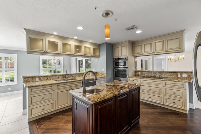 kitchen with pendant lighting, sink, a kitchen island with sink, double oven, and cream cabinets