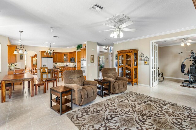 living room featuring light tile patterned floors, ornamental molding, ceiling fan with notable chandelier, and visible vents
