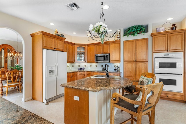 kitchen featuring sink, hanging light fixtures, a kitchen island with sink, a notable chandelier, and white appliances