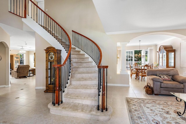 staircase featuring crown molding, a high ceiling, tile patterned flooring, baseboards, and arched walkways