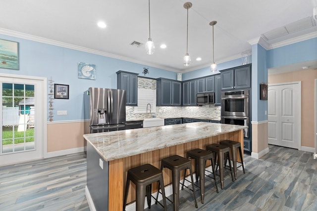 kitchen featuring pendant lighting, decorative backsplash, a kitchen island, light stone counters, and stainless steel appliances