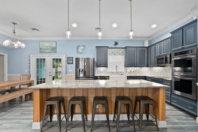 kitchen featuring stainless steel appliances, light stone countertops, a kitchen island, and pendant lighting