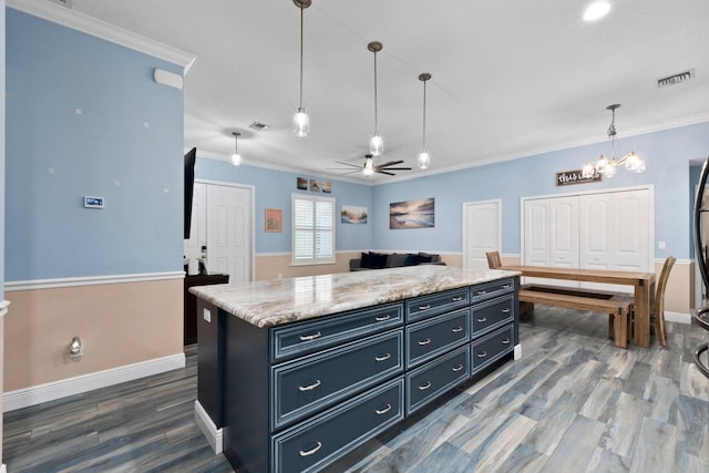 kitchen with dark wood-type flooring, ceiling fan, hanging light fixtures, a center island, and ornamental molding