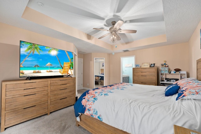 carpeted bedroom featuring a textured ceiling, connected bathroom, a tray ceiling, and ceiling fan