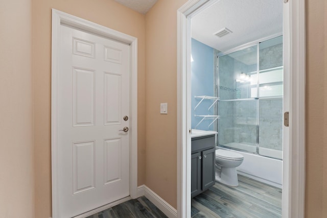 full bathroom with toilet, wood-type flooring, shower / bath combination with glass door, a textured ceiling, and vanity