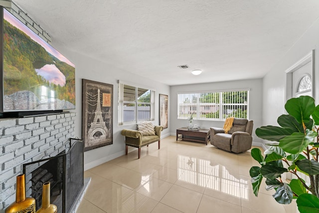 living room with light tile patterned flooring, a textured ceiling, and a brick fireplace