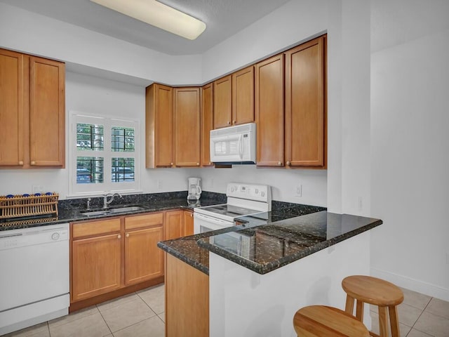 kitchen featuring light tile patterned flooring, white appliances, sink, dark stone countertops, and kitchen peninsula