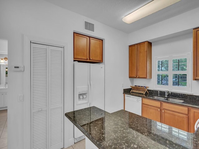 kitchen featuring light tile patterned flooring, dark stone countertops, white appliances, and sink